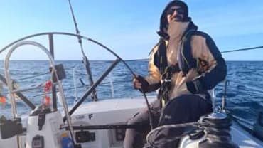 a yacht delivery skipper at the helm sailing in Asia, the picture shows the skipper holding the wheel and looking at the sails with flat water and blue sky