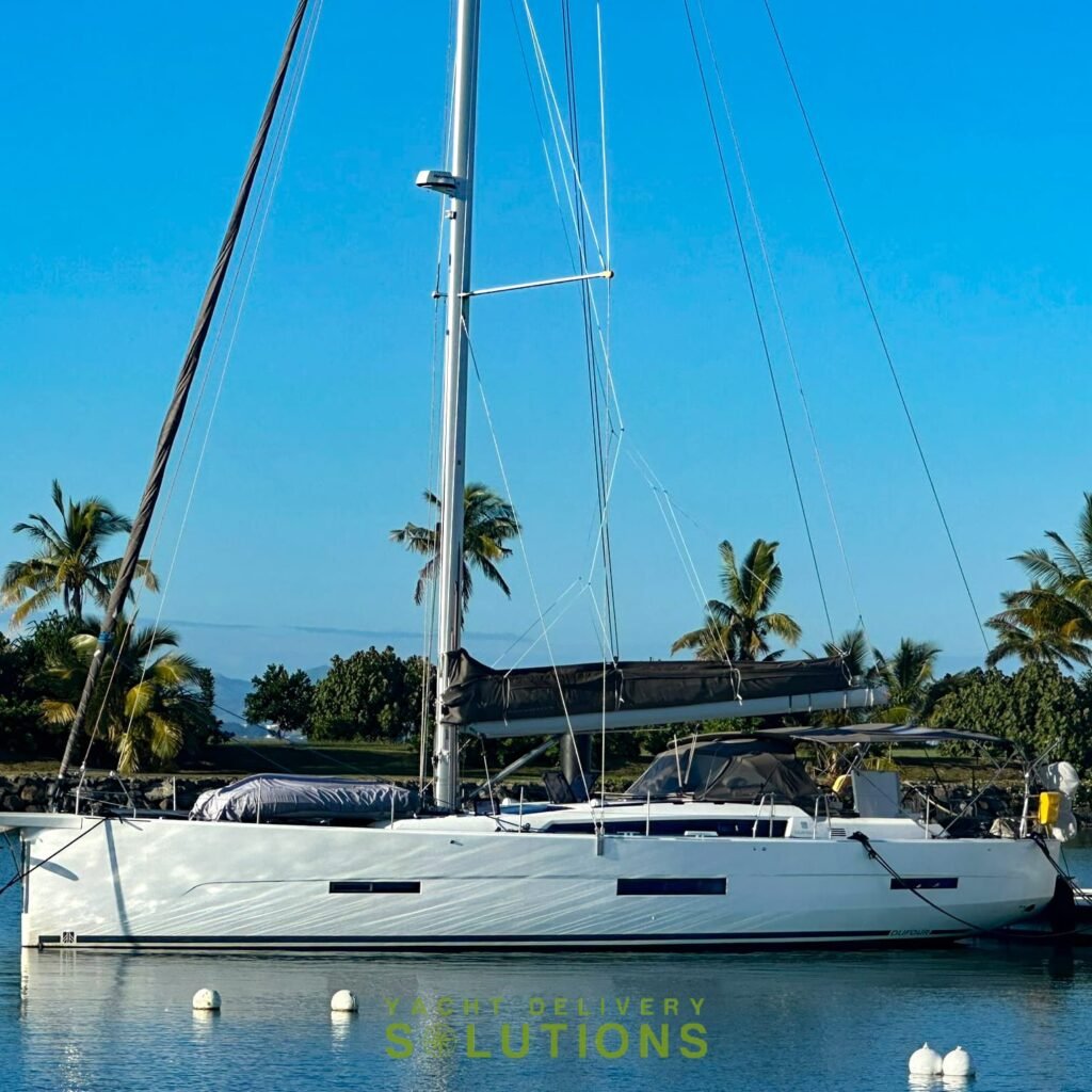 A white dufour 56 tied to the dock after the yacht delivery to Phuket. the sky is blue and the mast is white. the view shows the boat from the port side.