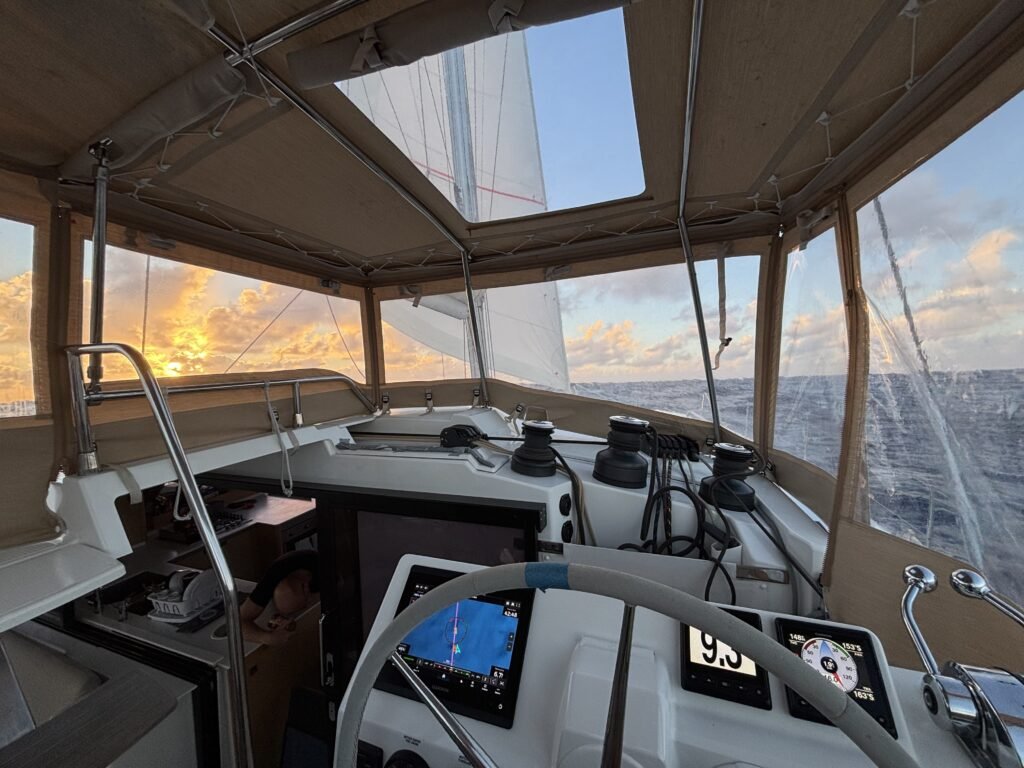 A Fountaine Pajot Tanna 47 on a yacht delivery the view shows the cockpit and instruments in the foreground and the beginning of a sunset to the right hand side. the yacht delivery skipper in Asia took the photo.