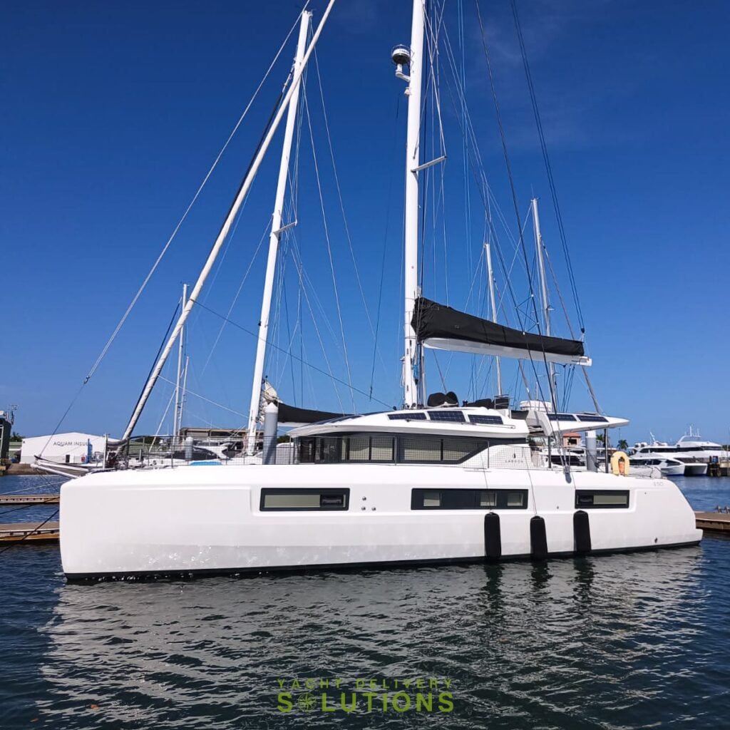 a white lagoon 50 catamaran with 3 black fenders hanging down the side, 3 black windows and a black sail cover. The sky is blue, the yacht delivery Skipper is behind the mast