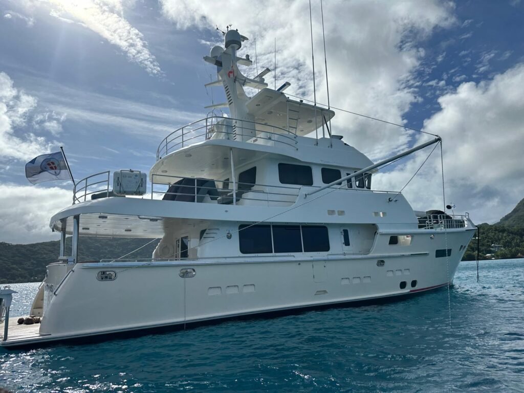 A cream colored Nordhavn 76 in Bora Bora being prepared by yacht delivery solutions a white could is visible and the water is clean and blue